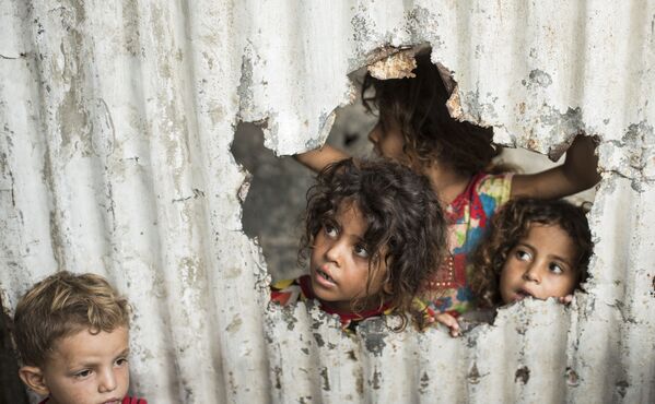 加沙一個貧民區，巴勒斯坦兒童通過金屬板柵欄上的口子向外看 - 俄羅斯衛星通訊社