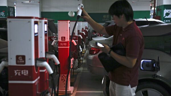 A man prepares to charge his electric-powered vehicle parked at a shopping mall in Beijing - 俄羅斯衛星通訊社
