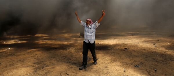 A Palestinian man walks in the smoke billowing from burning tyres during clashes with Israeli forces along the border with the Gaza strip east of Khan Yunis - 俄羅斯衛星通訊社