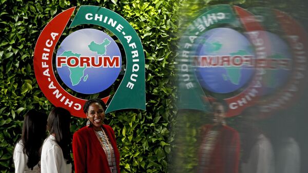 An African delegate talks with the Chinese women as they walk by the logo of the Forum on China-Africa Cooperation on display at the venue in Beijing - 俄羅斯衛星通訊社