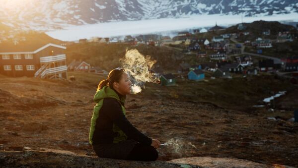 年轻的女孩坐在石头上，在落日的余晖中抽烟，塔西拉克镇（Tasiilaq Town），格陵兰岛 - 俄罗斯卫星通讯社