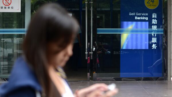 A woman looks at her mobile phone as she walks past a bank in Beijing - 俄羅斯衛星通訊社