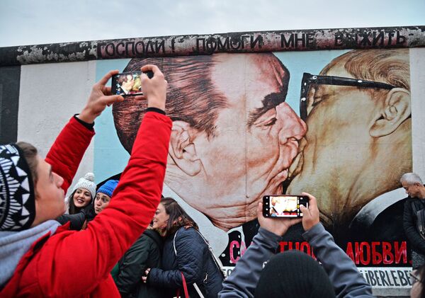 人们在磨坊街（Mühlenstrasse）柏林墙艺术作品展示区Dmitri Wrubel绘制的《我的上帝，助我在这致命之爱中存活》或称《兄弟之吻》的画作旁 - 俄罗斯卫星通讯社