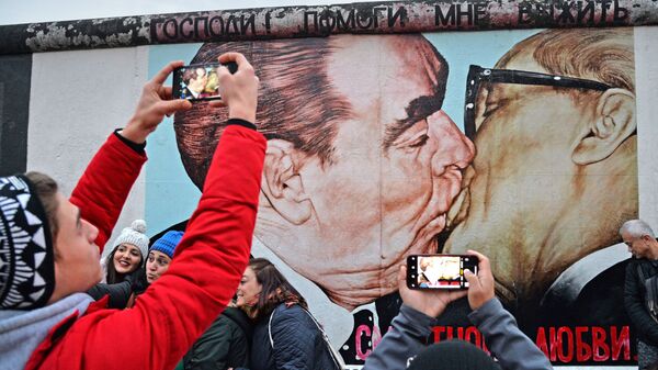 人们在磨坊街（Mühlenstrasse）柏林墙艺术作品展示区Dmitri Wrubel绘制的《我的上帝，助我在这致命之爱中存活》或称《兄弟之吻》的画作旁 - 俄罗斯卫星通讯社