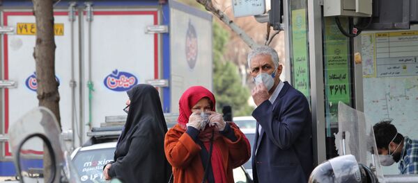 People wearing protective masks wait along the side of a street in the Iranian capital Tehran  - 俄羅斯衛星通訊社