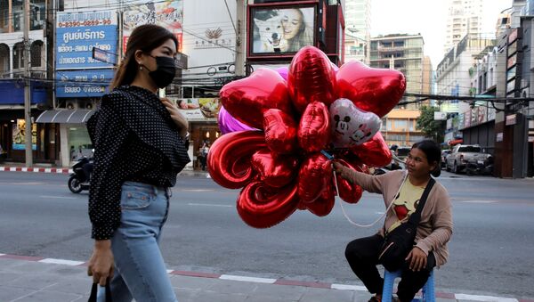 Женщина в медицинской маске проходит мимо продавщицы воздушных шаров накануне Дня святого Валентина в Бангкоке, Таиланд  - 俄罗斯卫星通讯社