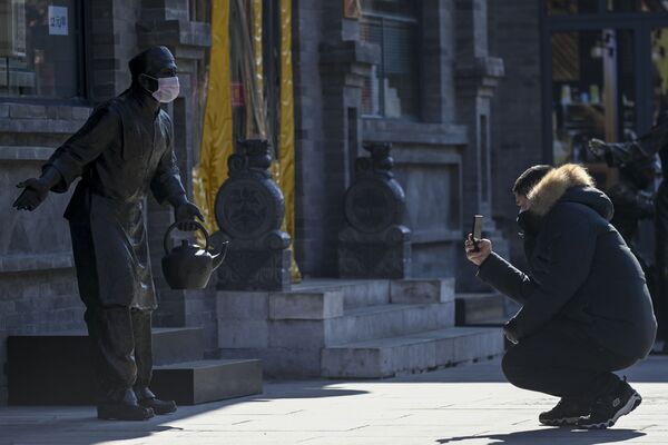 Мужчина фотографирует статую в защитной маске, Пекин - 俄羅斯衛星通訊社