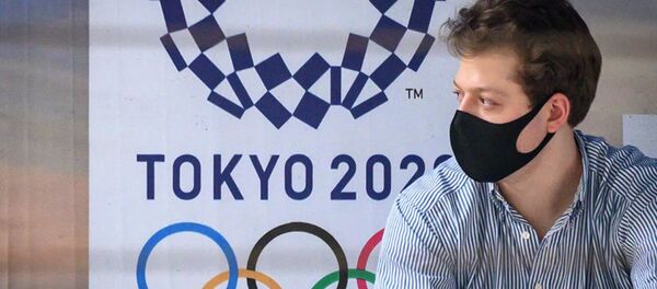 Мужчина в маске на фоне лого олимпийских игр в Японии Мужчина в маске на фоне лого олимпийских игр в Японии - 俄罗斯卫星通讯社