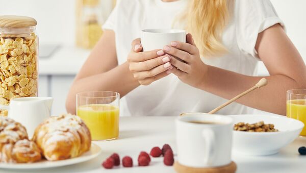 Женщина с чашкой кофе и завтраком на столе - 俄羅斯衛星通訊社
