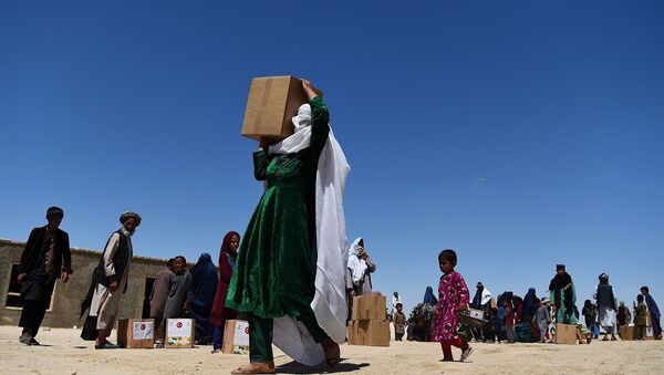 n this photograph taken on May 3, 2020, an internally displaced woman carries free aid over her shoulders distributed during the Holy month of Ramadan in a refugee camp on the outskirts of Mazar-i-Sharif. (Photo by FARSHAD USYAN / AFP) - 俄罗斯卫星通讯社