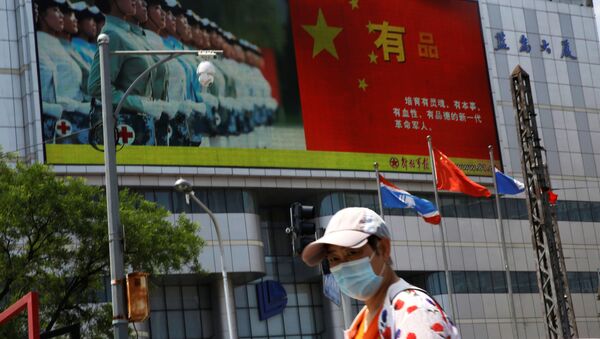 A pedestrian wearing a face mask walks past a screen showing an image of Chinese People's Liberation Army - 俄羅斯衛星通訊社