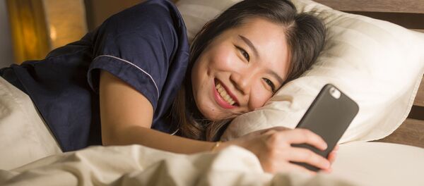 Молодая улыбающаяся японская девушка во время использования смартфона  - 俄罗斯卫星通讯社